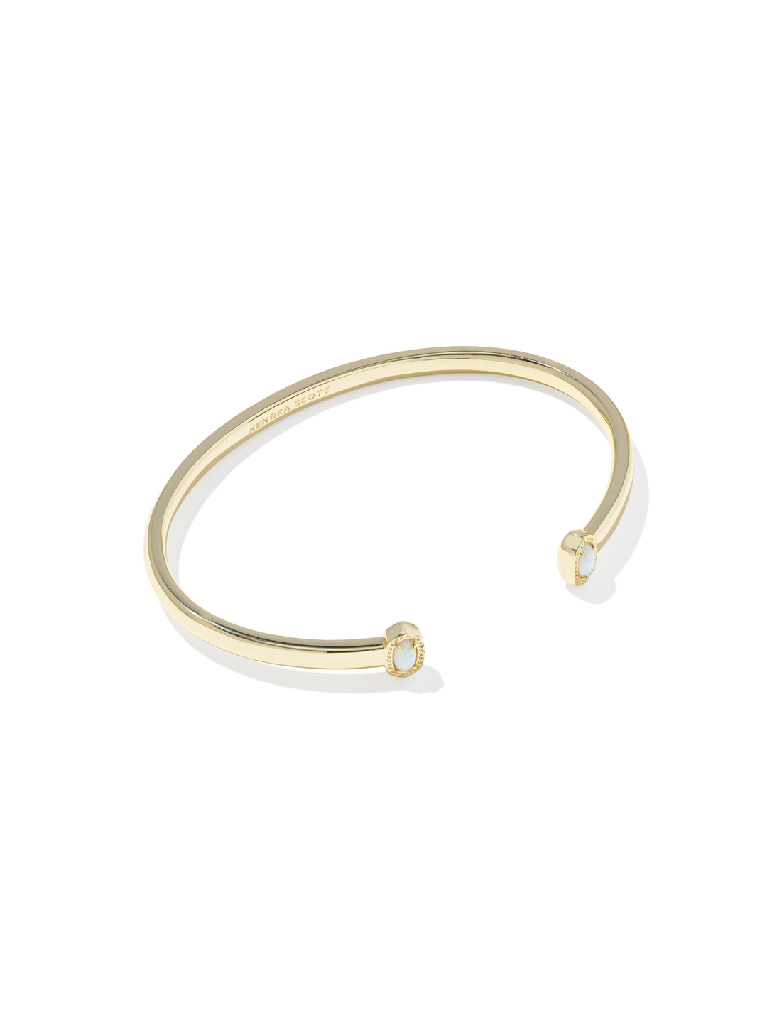 A slim gold-tone open cuff bangle bracelet with a small oval clear stone set in each end, shown on a clean white background.
