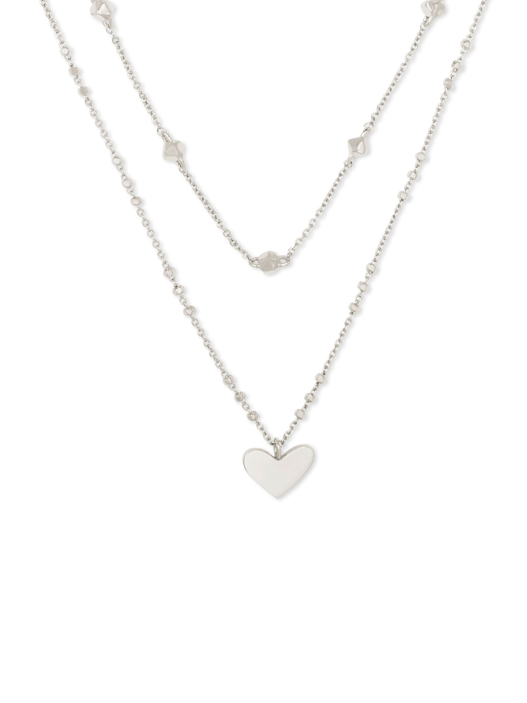 A silver double-layered necklace featuring a delicate chain with small star-shaped charms and a longer chain with a polished heart pendant, displayed against a solid white background.