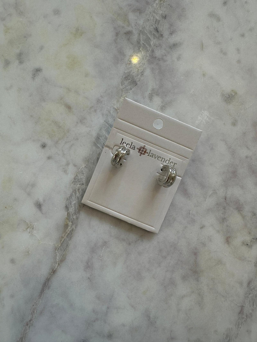 Pair of silver earrings on a branded card on a marble surface