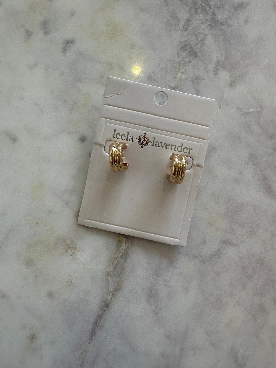Gold earrings on a Leela Lavender card against a marble background