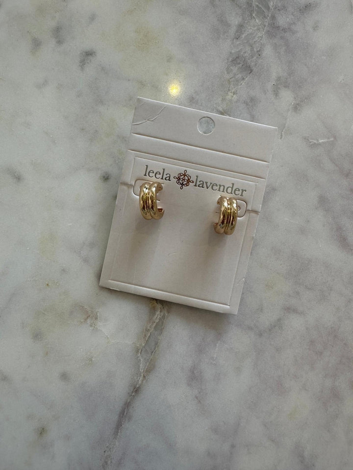 Gold earrings on a Leela Lavender card against a marble background