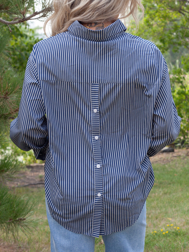 A person viewed from behind wearing a navy and white vertically striped button-down shirt and light blue jeans in an outdoor garden setting.