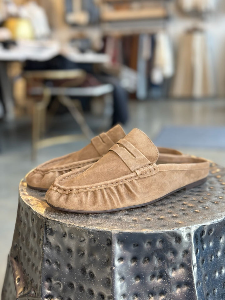 Pair of tan loafers on a textured metal stool with a blurred indoor background