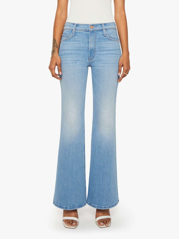 A model wearing light blue high-waisted flare jeans with a subtle fade wash, paired with a white top and white heeled sandals, shown against a plain white background.