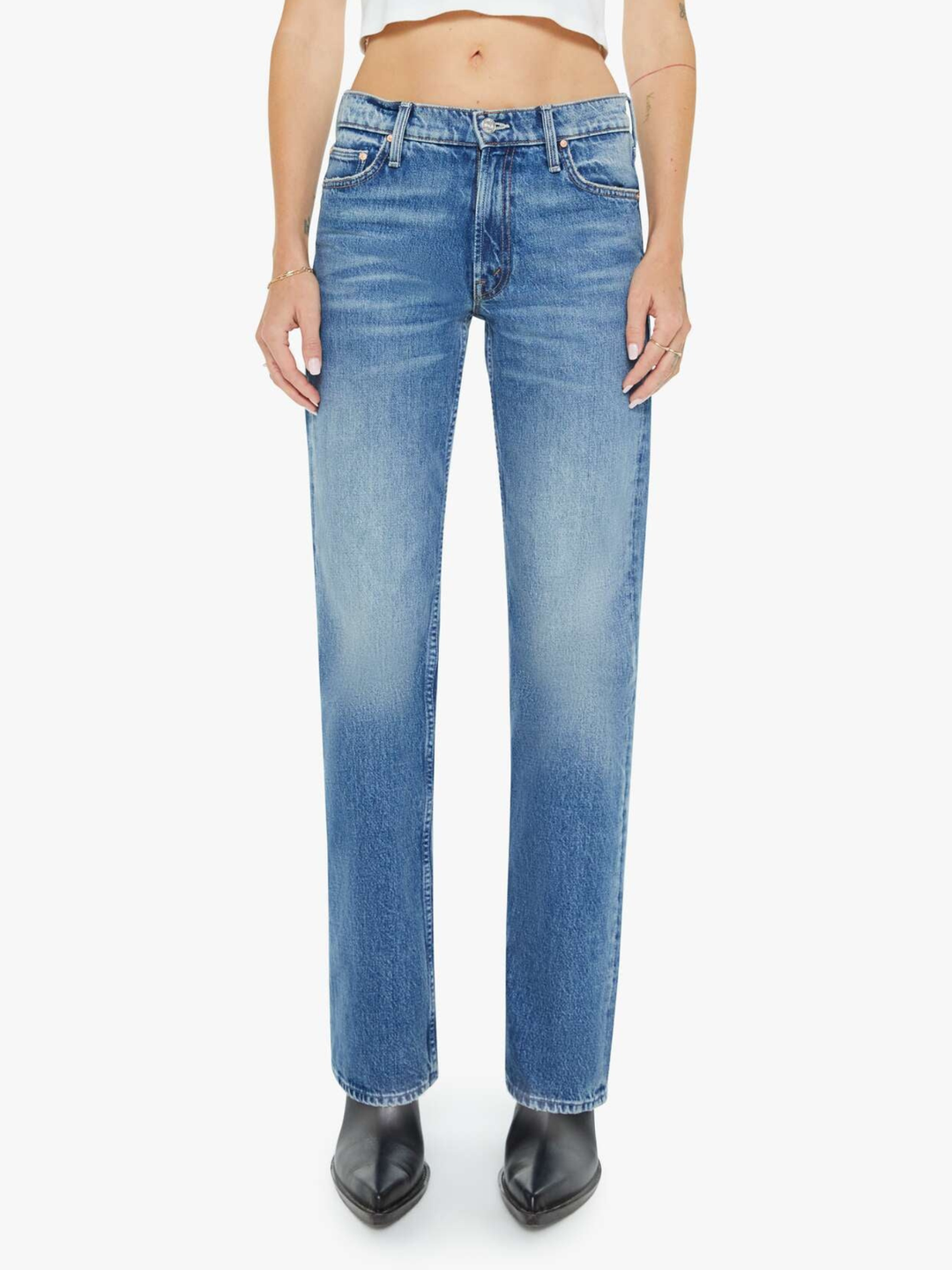 A model wearing a pair of medium-wash blue denim jeans with a subtle vertical fade, paired with black pointed-toe boots against a plain white background.