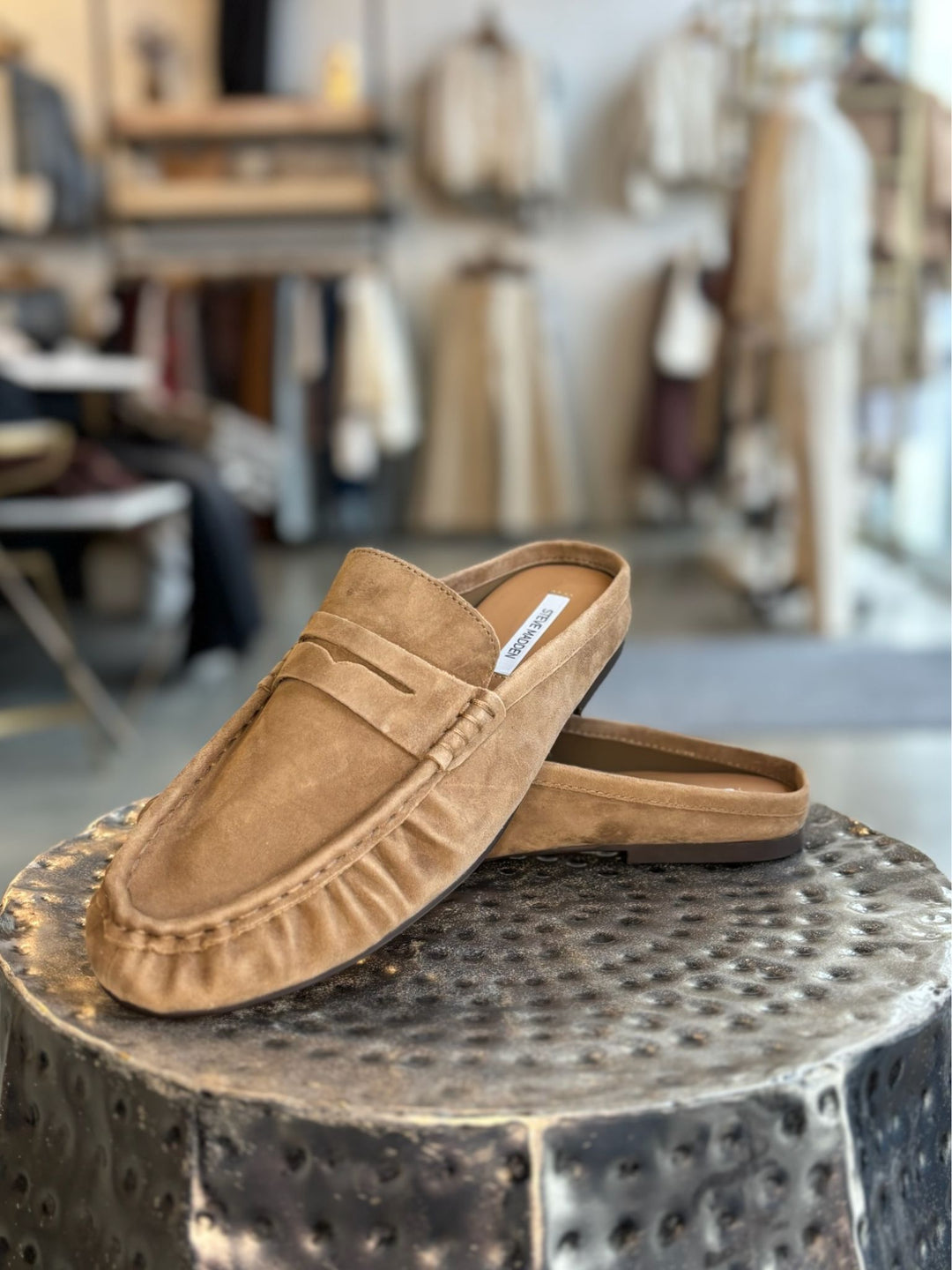 Pair of tan loafers on a textured metal stool with a blurred indoor background