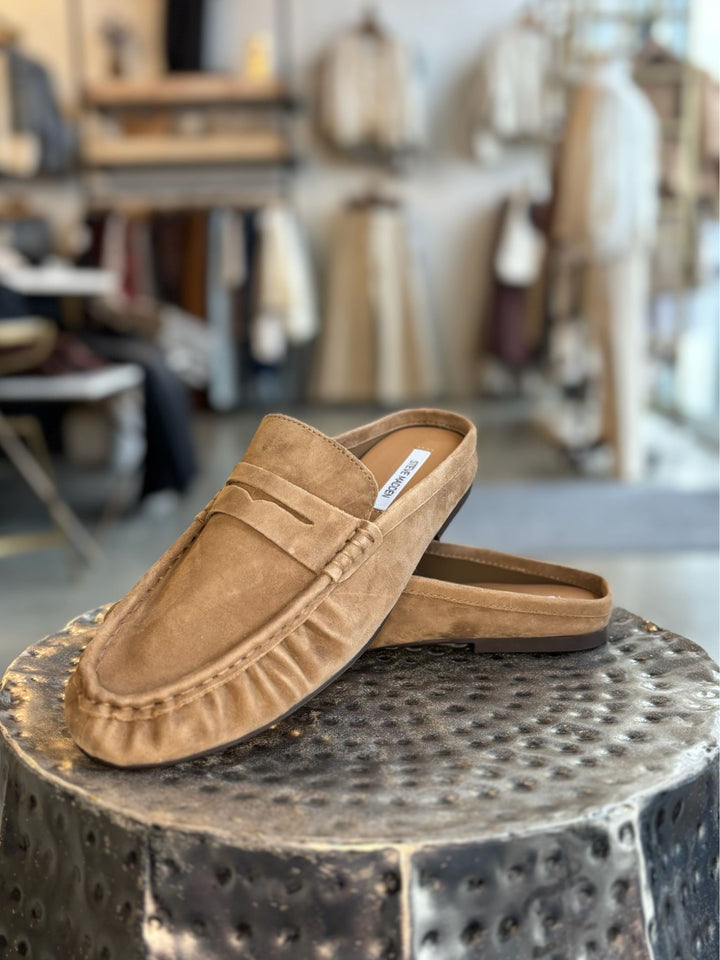 Pair of tan loafers on a textured metal stool with a blurred indoor background