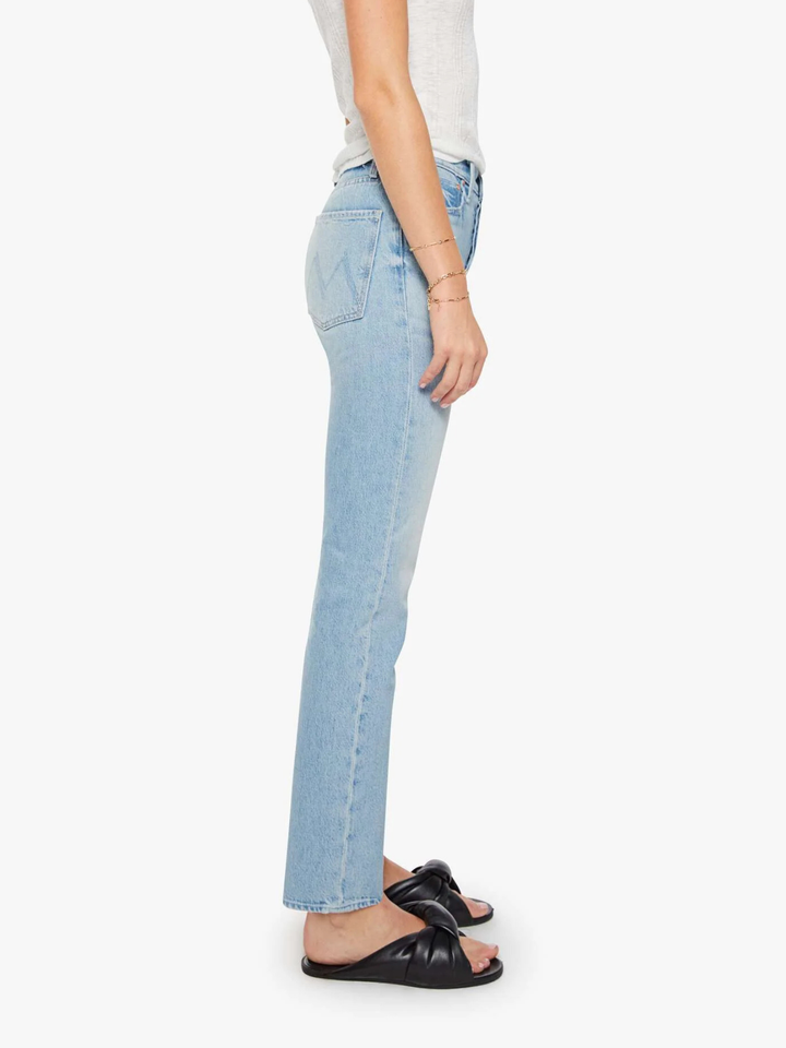 A side profile view of a model wearing light-wash blue denim jeans, a white top, and black slide sandals against a plain white background.