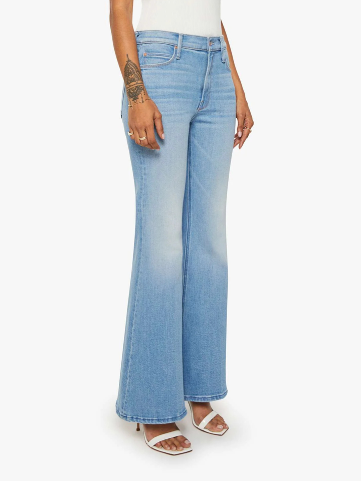 A model wearing light blue high-waisted flare jeans with a faded wash, styled with a white top and white heeled sandals against a plain white background.