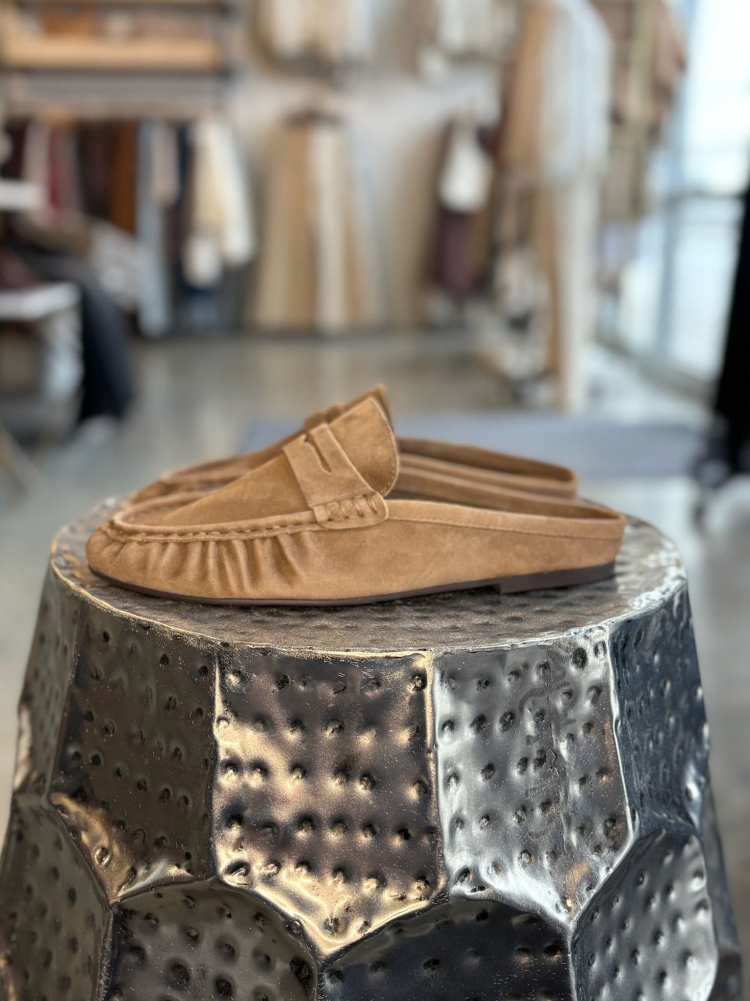 Pair of tan loafers on a textured metal stool with a blurred indoor background