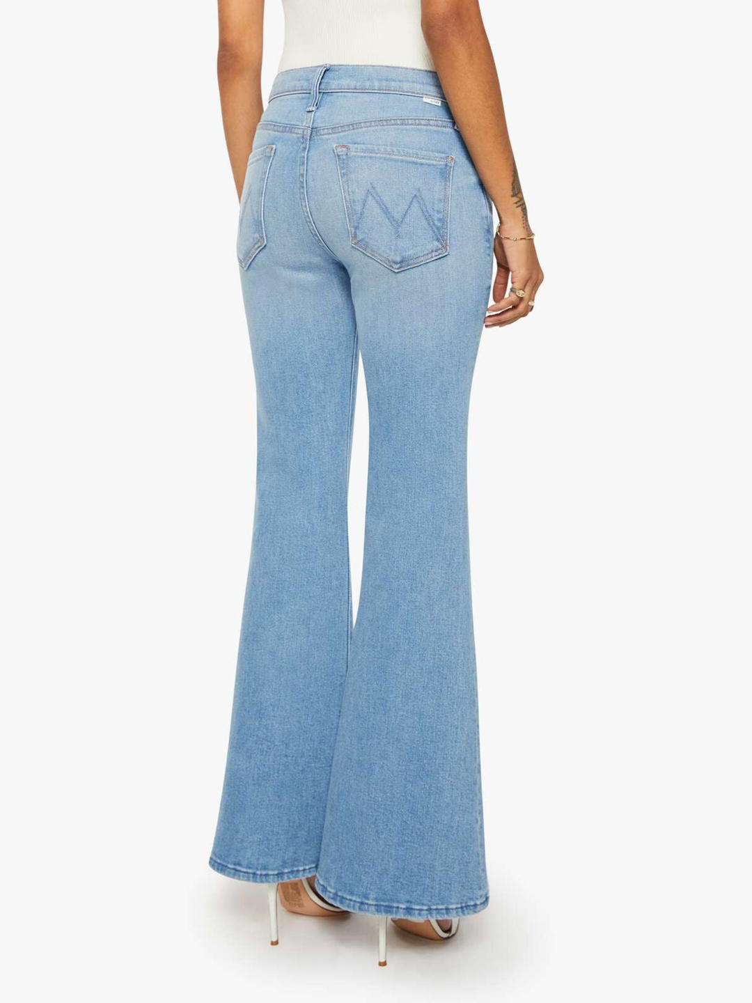 A person shown from the back wearing light-wash blue flare jeans with a white top and clear high-heeled sandals against a plain light background.