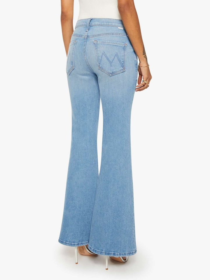A person shown from the back wearing light-wash blue flare jeans with a white top and clear high-heeled sandals against a plain light background.