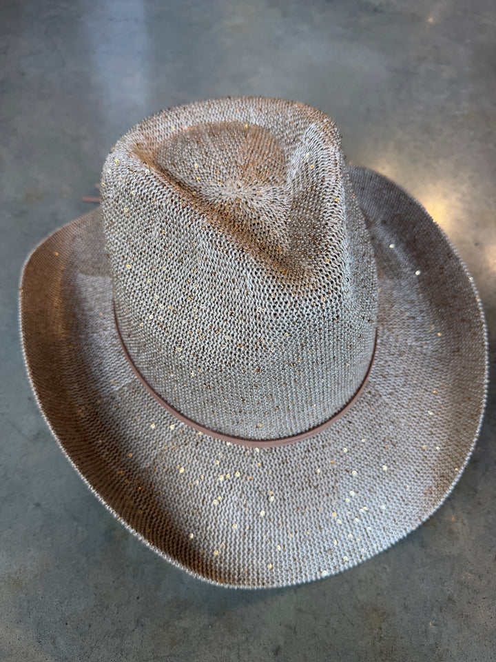 A light beige straw cowboy hat embellished with small silver glitter beads, displayed on a gray concrete floor.