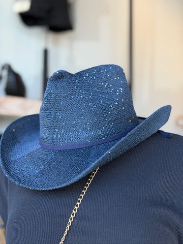 A blue woven cowboy hat with silver glitter accents and a matching blue band, resting on a navy blue ribbed sweater with a gold chain strap visible.