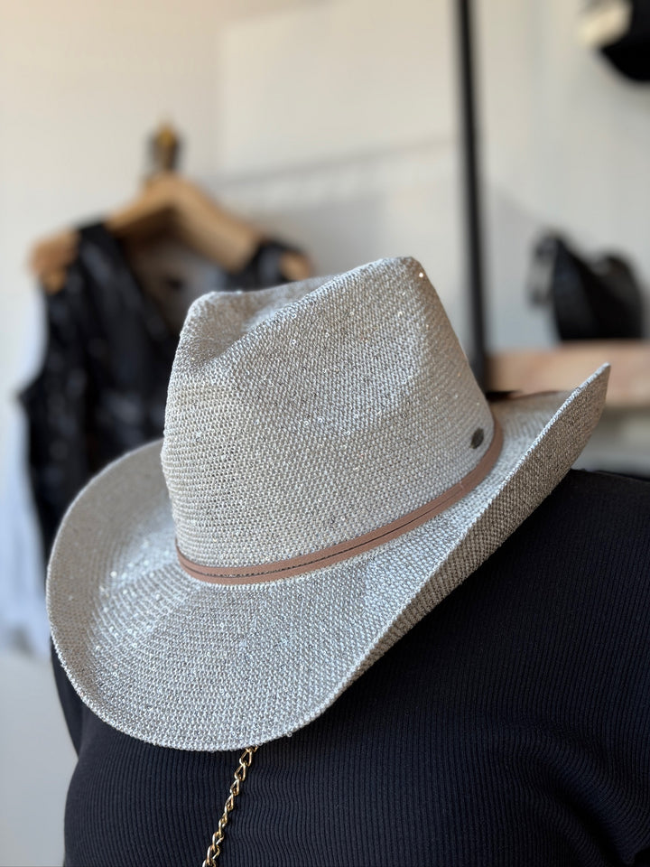 A textured silver straw cowboy hat with a thin tan band, shown from a side-back angle resting on a black mannequin torso in a store setting.