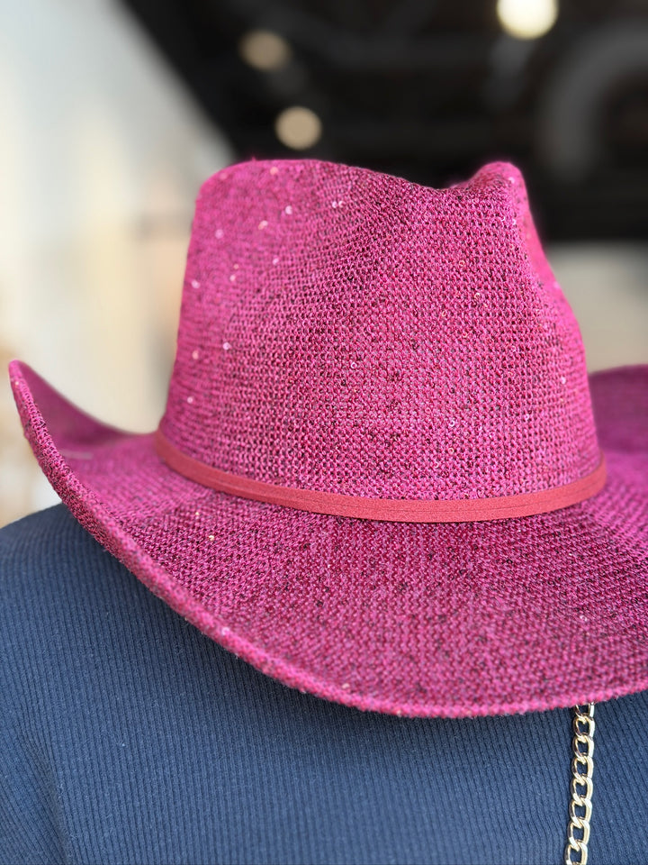 A close-up of a bright pink glitter cowboy hat with a matching pink band, displayed on a blue mannequin torso.