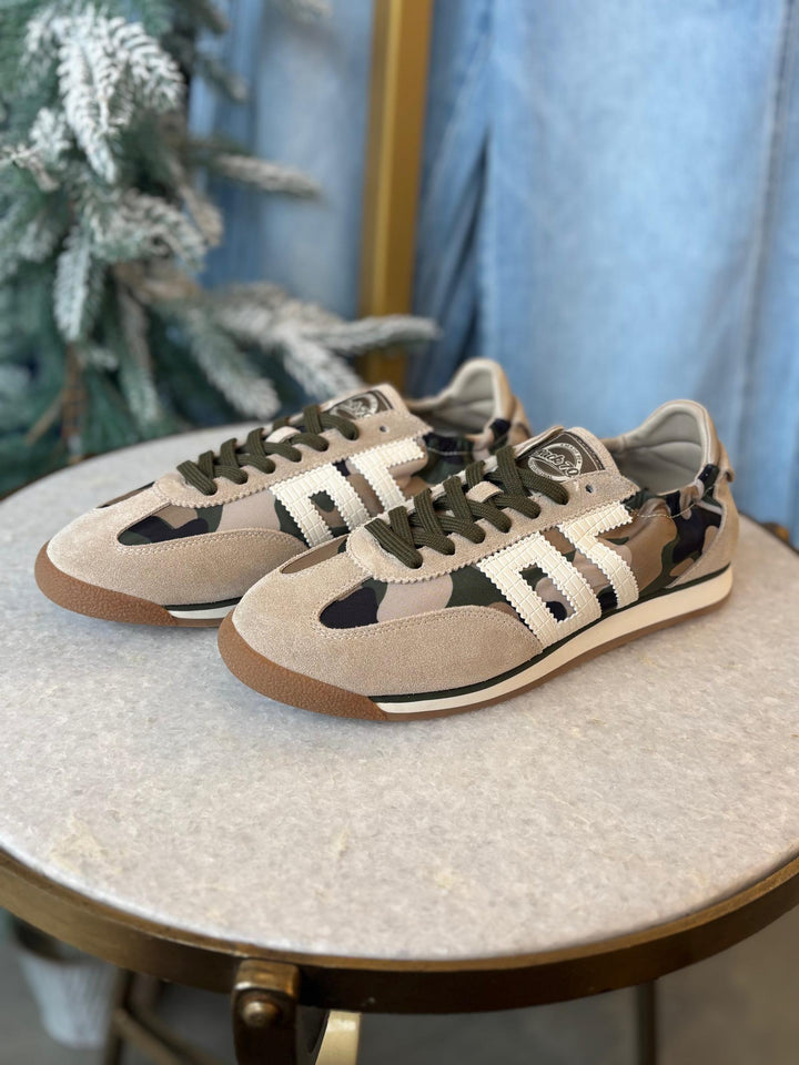 Camouflage sneakers on a round table with a decorative plant in the background