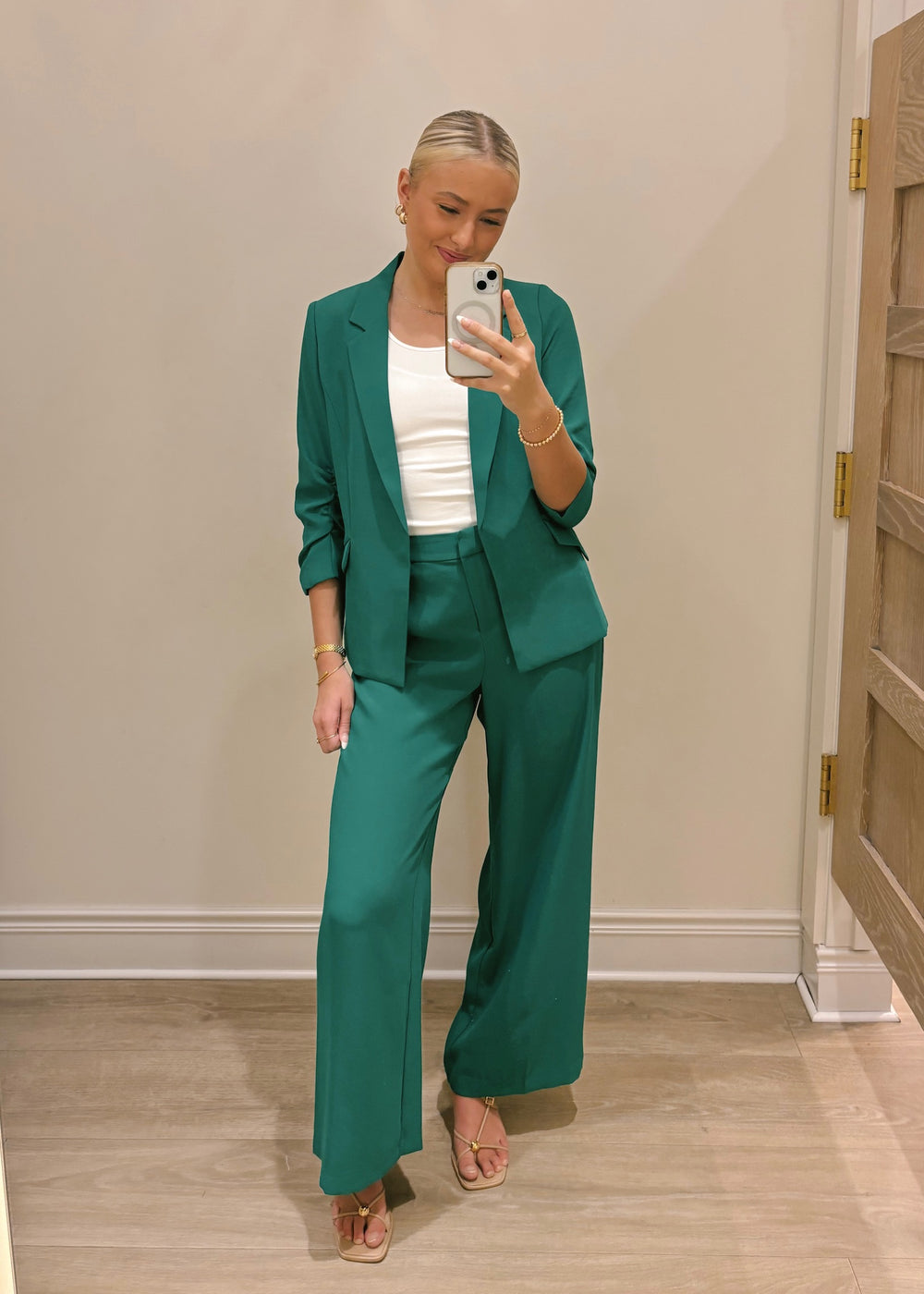 Woman taking a mirror selfie wearing a green suit and white top.