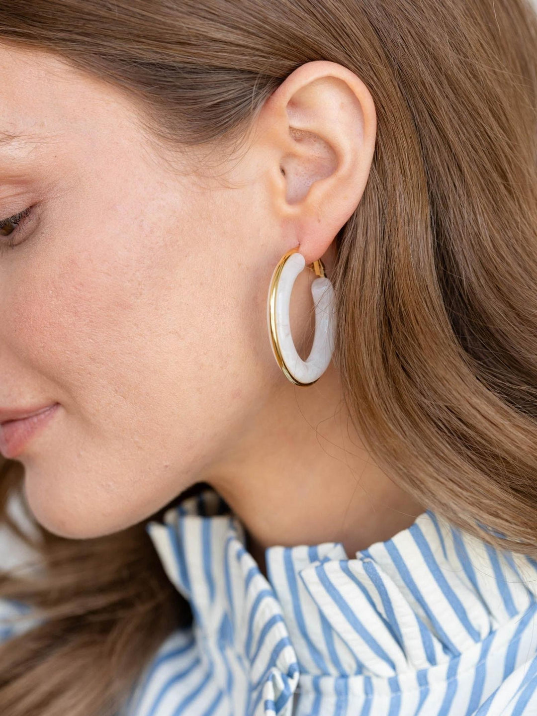 Close-up of a person wearing a gold hoop earring with a white stone.