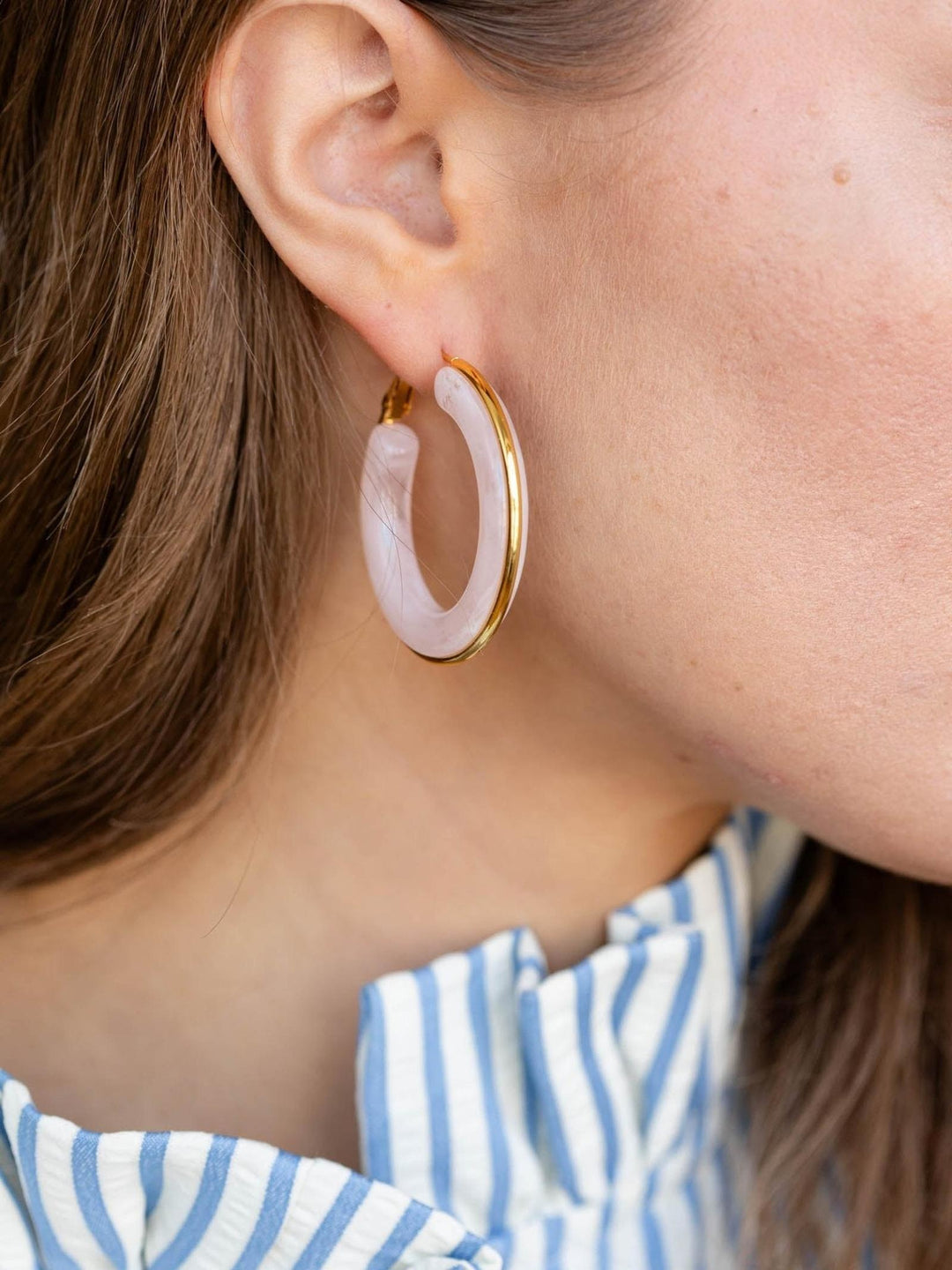 Close-up of an ear wearing a gold hoop earring with a pink stone.
