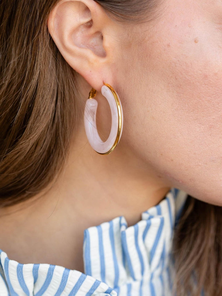 Close-up of an ear wearing a gold hoop earring with a pink stone.