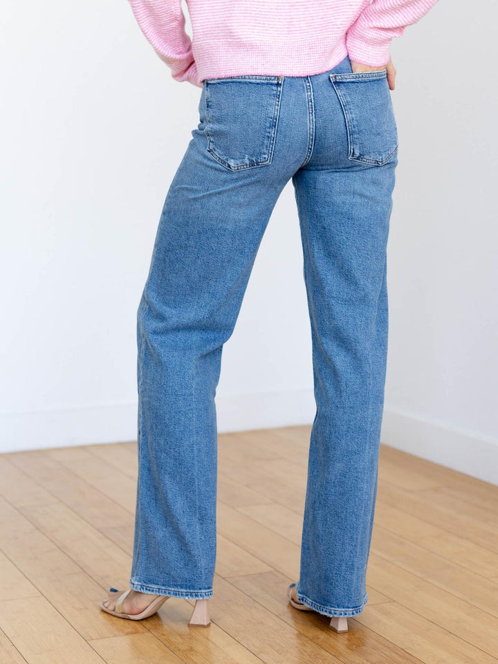 Person wearing blue jeans and a pink shirt on a wooden floor with a white wall background