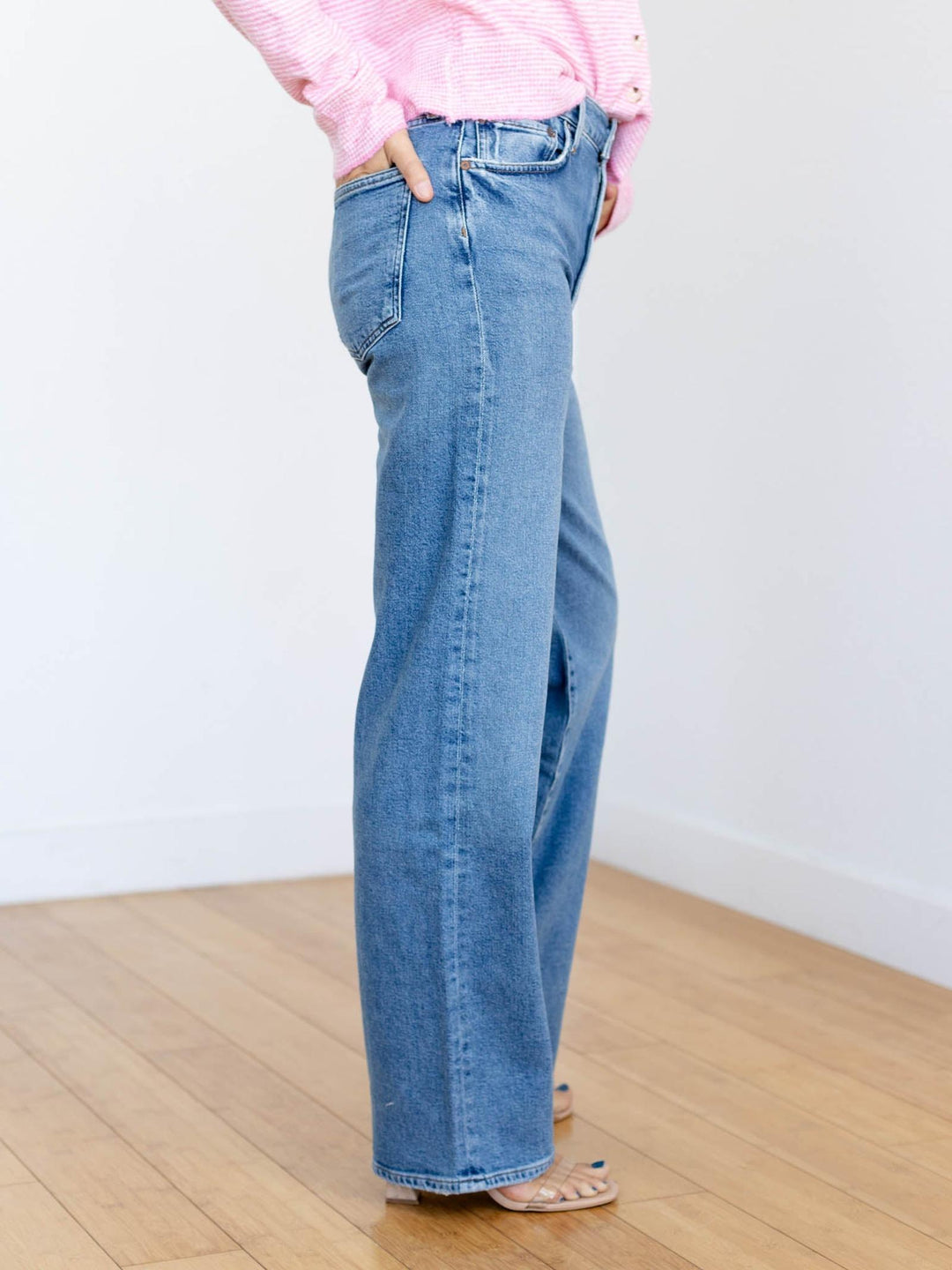 Person wearing blue jeans and a pink top against a white wall.