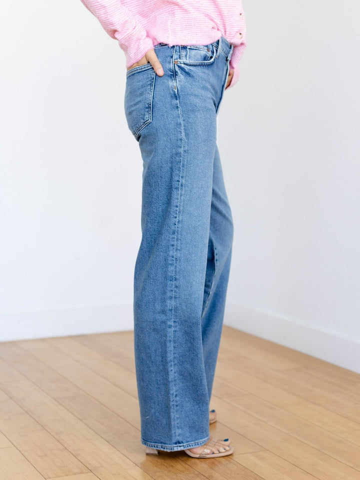 Person wearing blue jeans and a pink top against a white wall.