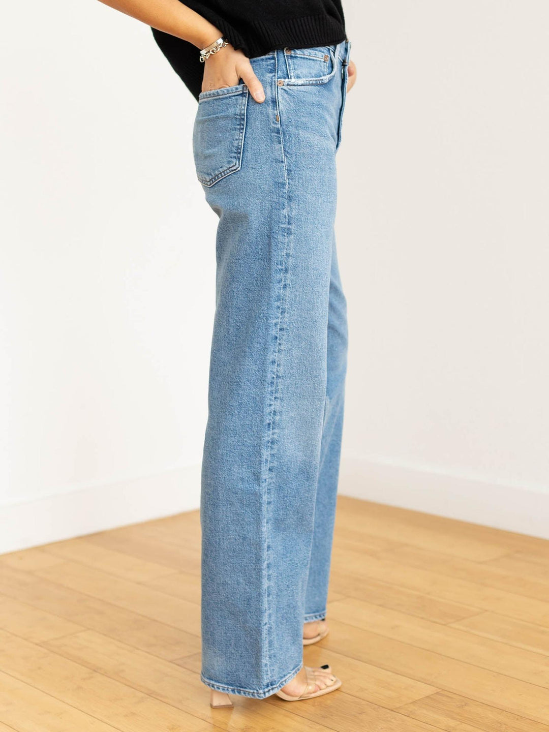 Person wearing light blue jeans on a wooden floor with a white wall background