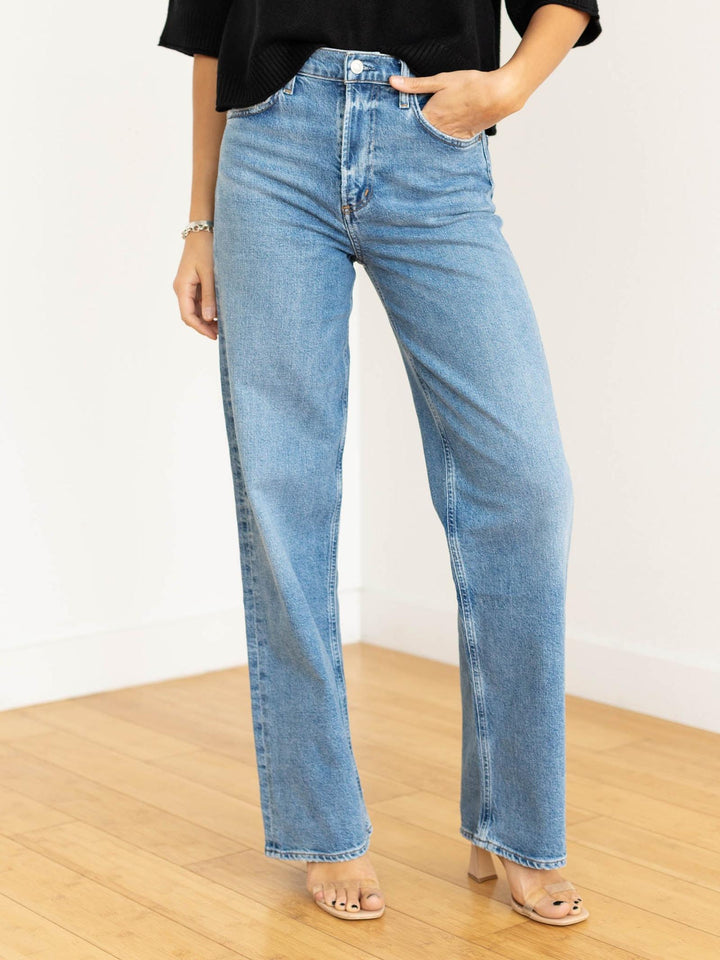 Person wearing light blue jeans on a wooden floor with a white wall background