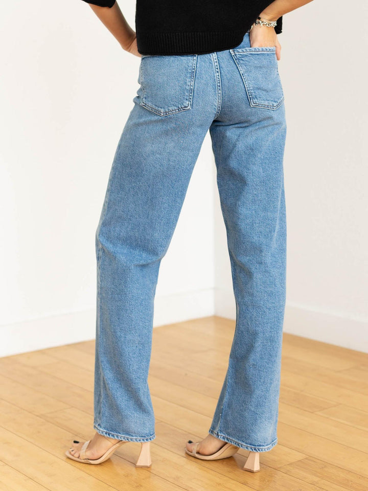 Person wearing light blue jeans on a wooden floor with a white wall background