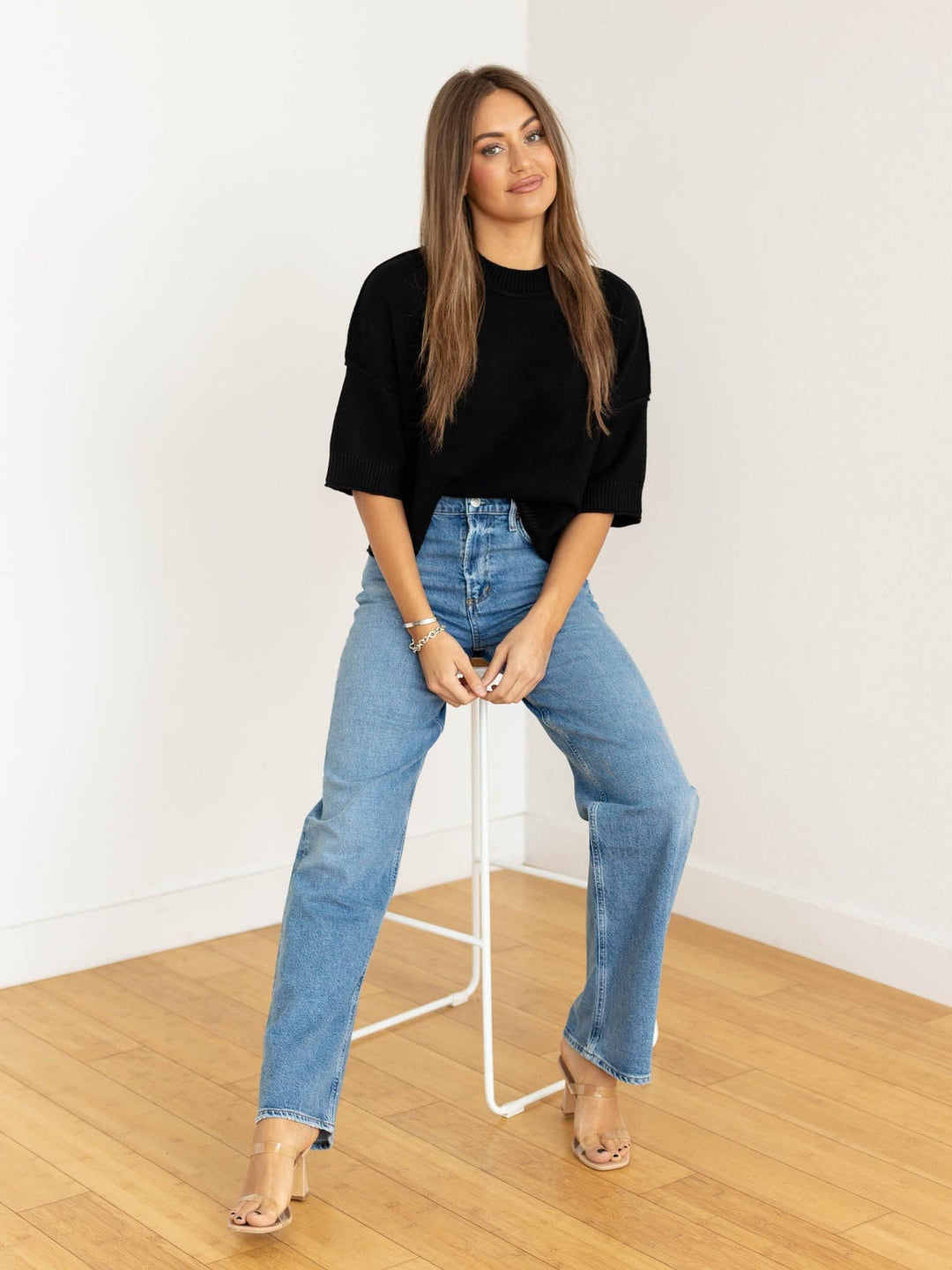 Woman wearing a black top and blue jeans standing in a minimalistic room.