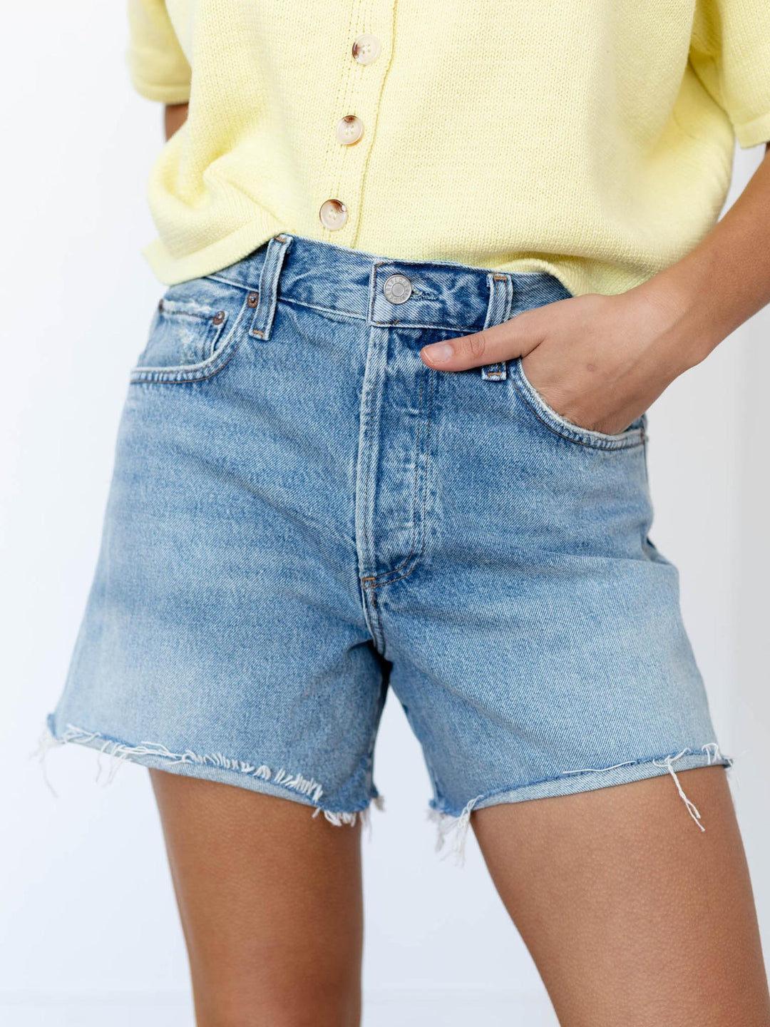 Person wearing light blue denim shorts and a yellow cardigan on a white background
