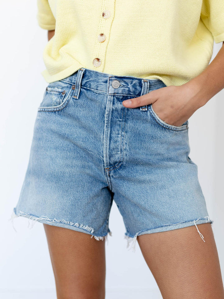 Person wearing light blue denim shorts and a yellow cardigan on a white background