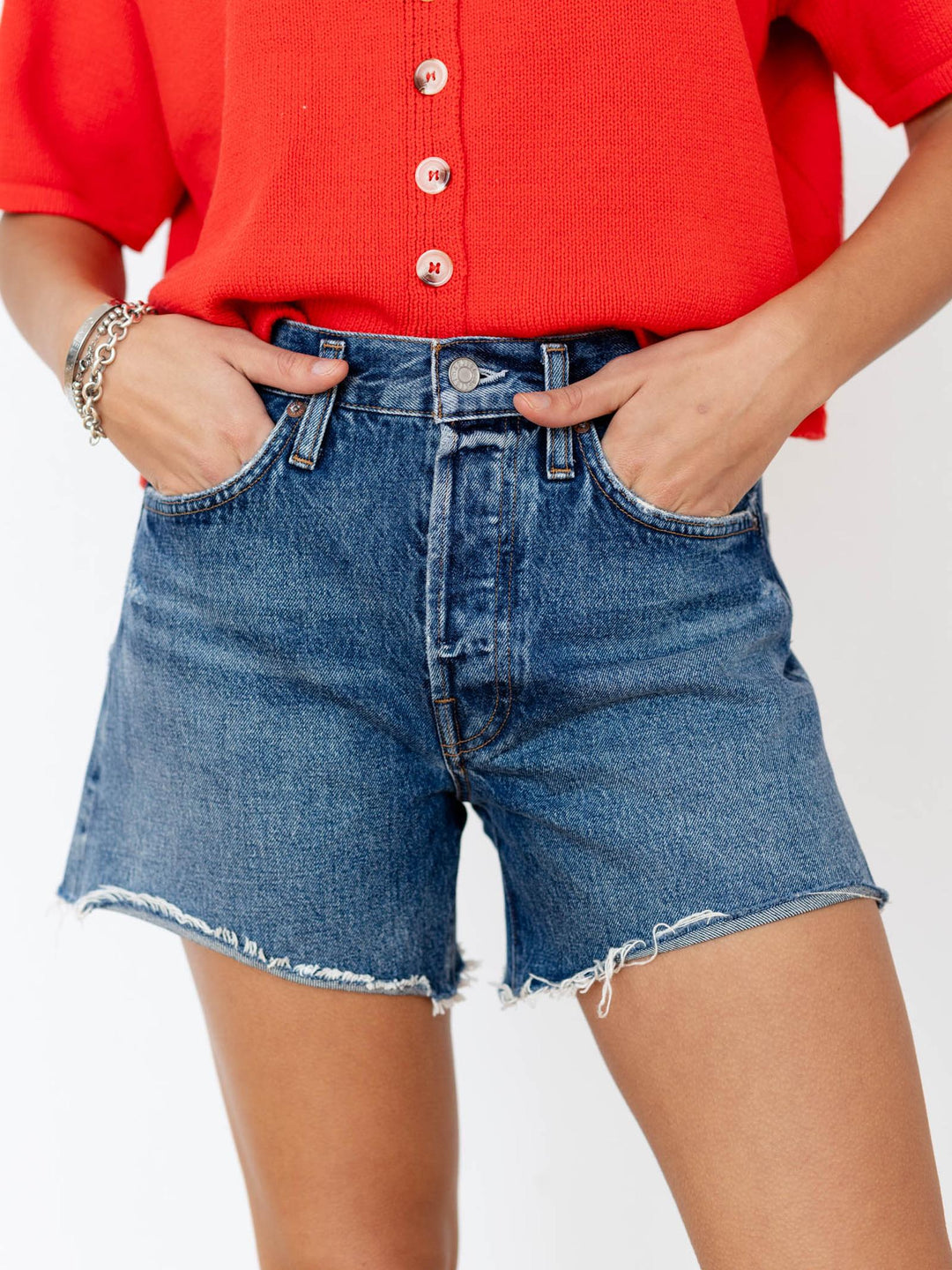 Person wearing a red button-up shirt and blue denim shorts on a white background