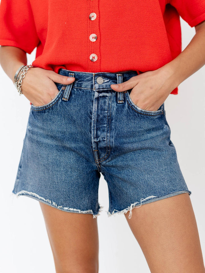 Person wearing a red button-up shirt and blue denim shorts on a white background
