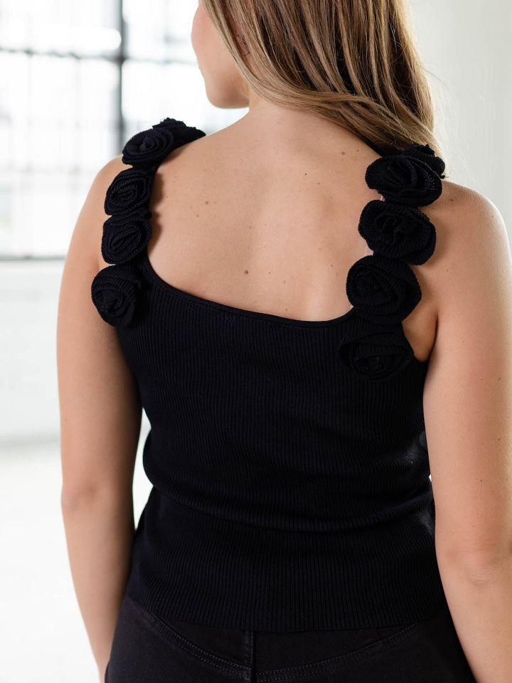 Black ribbed knit tank with delicate floral appliqué straps, seen from the back on a model.