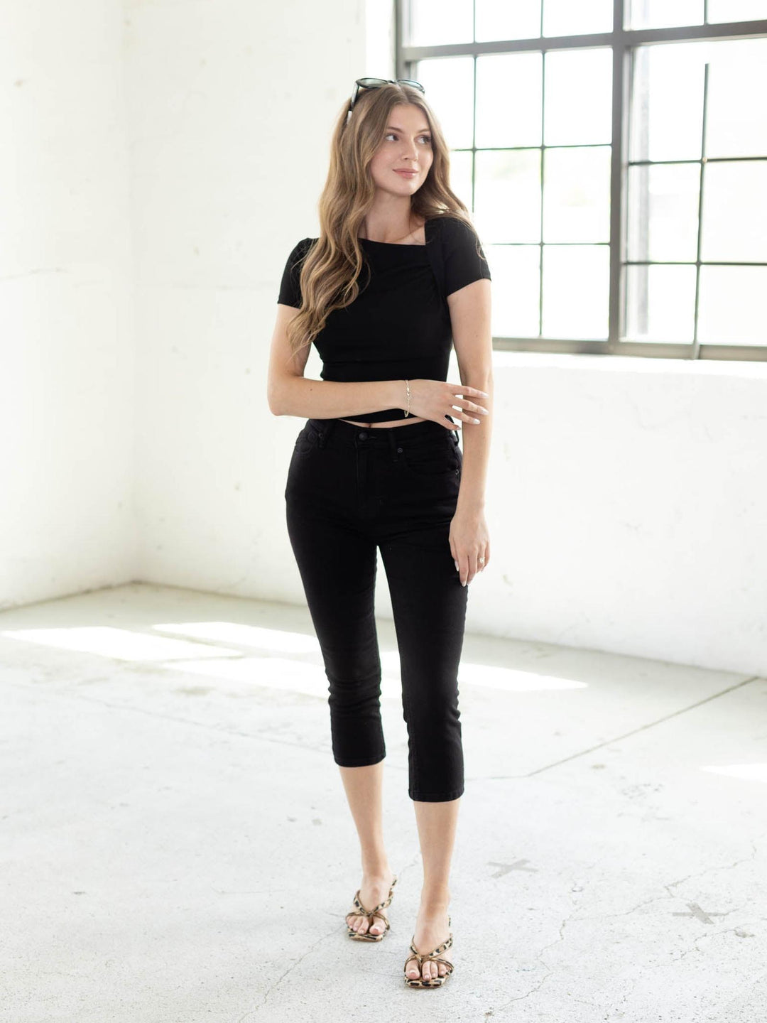 Model in a black asymmetrical ruched neckline short sleeve knit top, black capri pants, and studded sandals.
