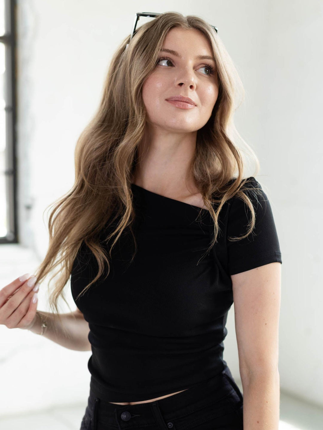 Woman in a fitted black ribbed knit top with an asymmetrical ruched neckline and capped short sleeves.