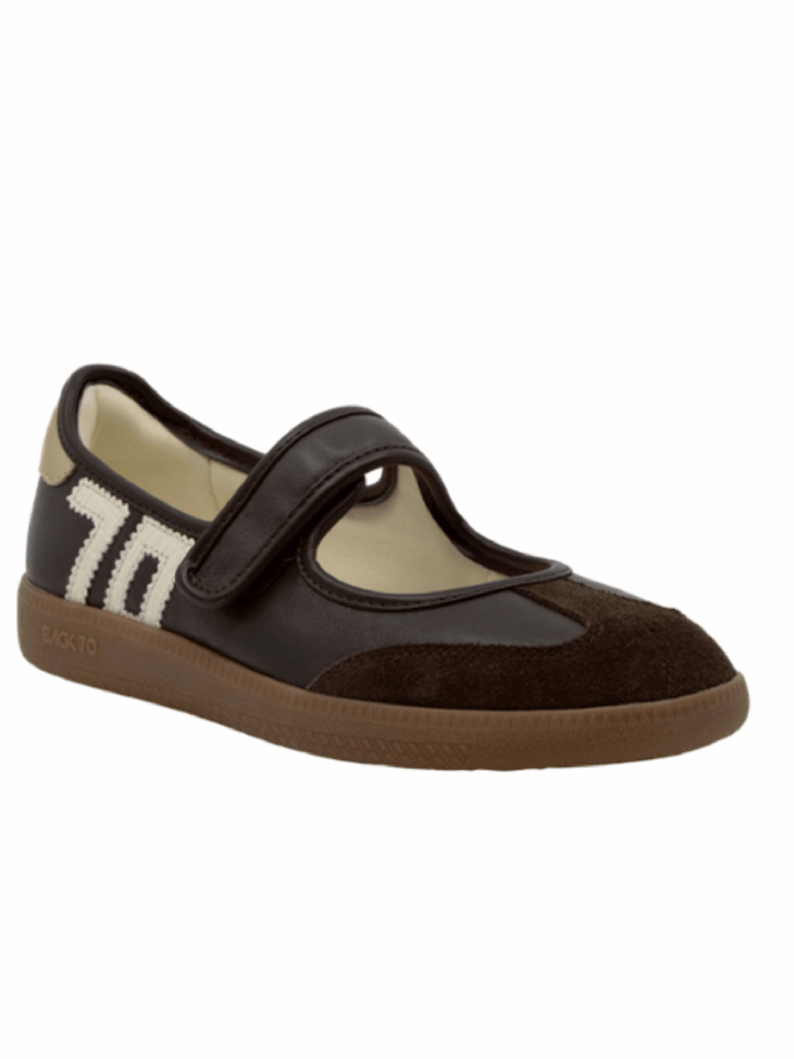 A dark brown and black Mary Jane style shoe with a hook-and-loop strap, a cream-colored interior lining, and a brown sole, shown against a plain white background.
