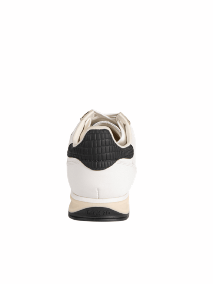 A single white leather sneaker shown from the rear, featuring a black textured heel counter and a beige midsole, set against a plain white background.