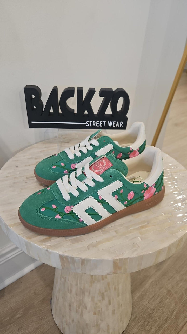 Green sneakers with floral patterns on a wooden stool, branded &