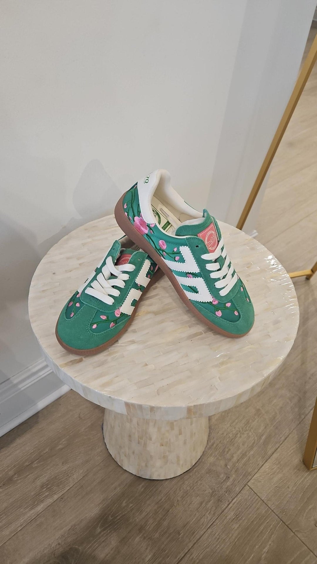 Green and white sneakers on a round wooden table against a white wall.