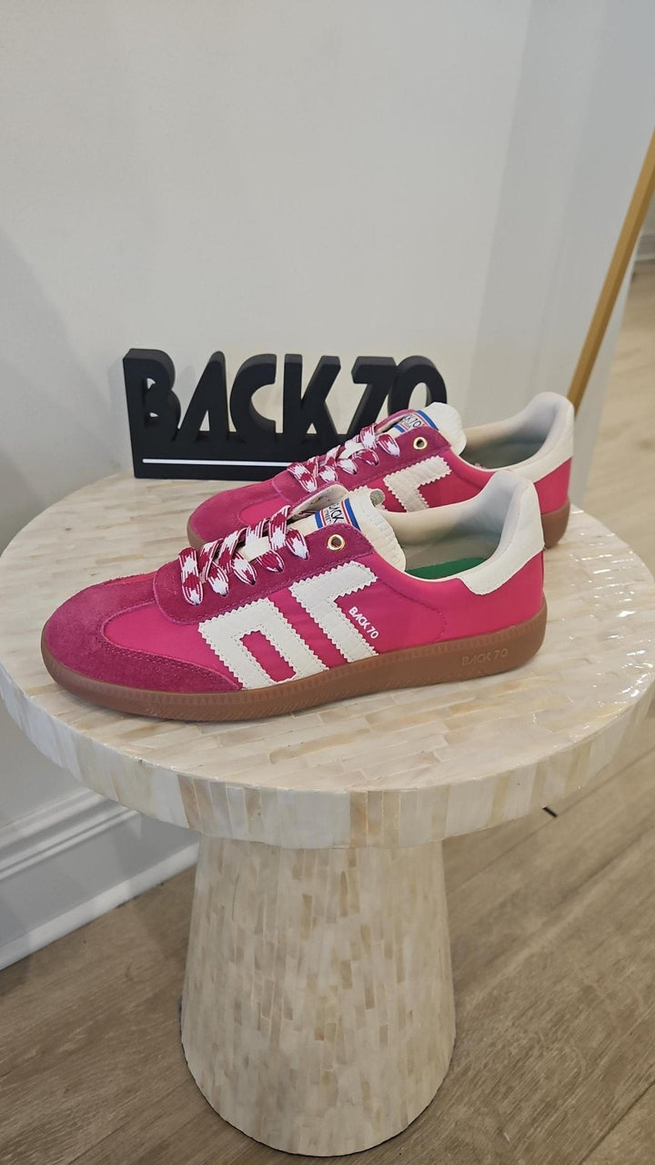 Pink sneakers with white accents on a wooden stool against a white wall with &