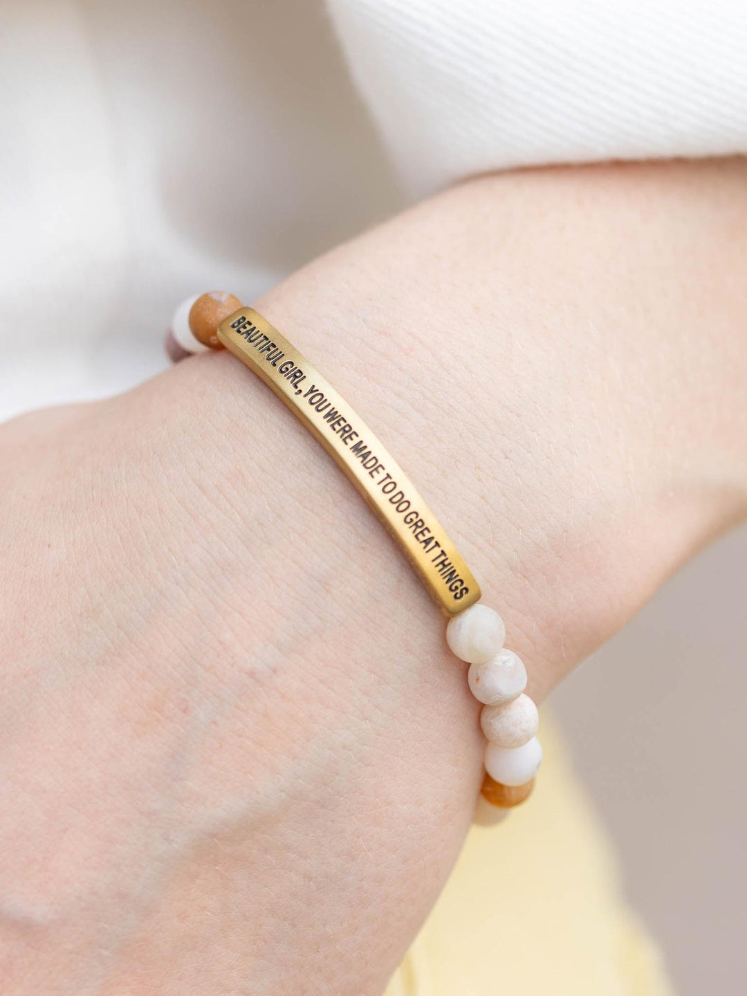 Hand wearing a "Beautiful Girl" stone bracelet with light pink and white beads, and a gold bar.