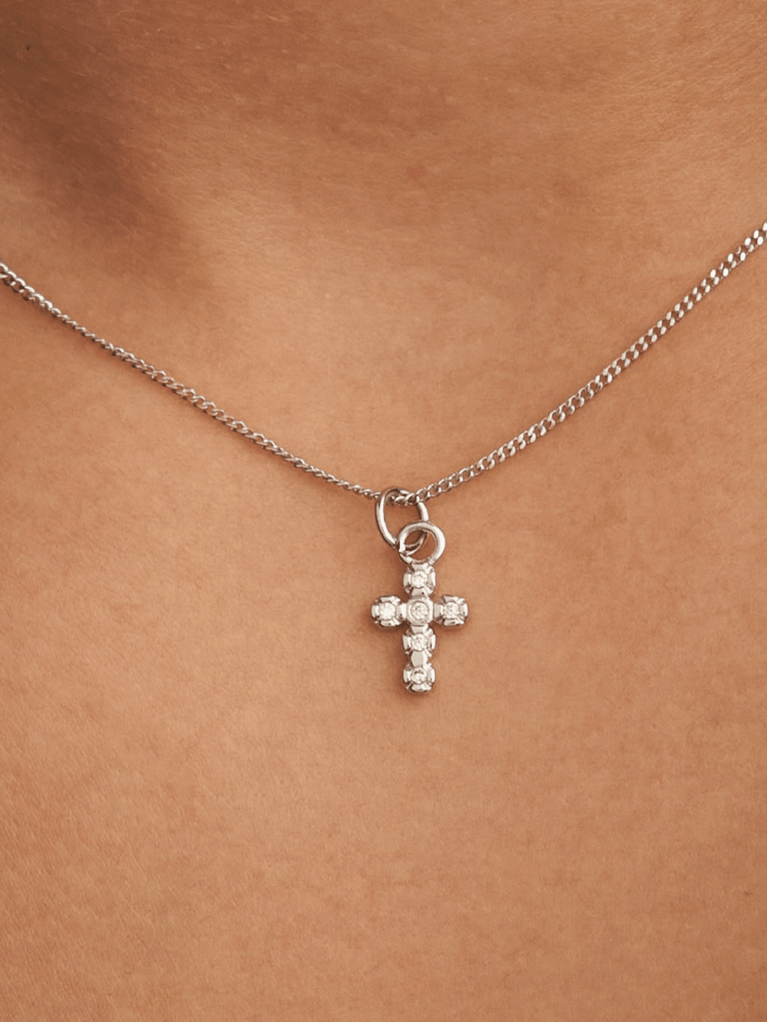 Silver cross necklace with clear stones on a person&