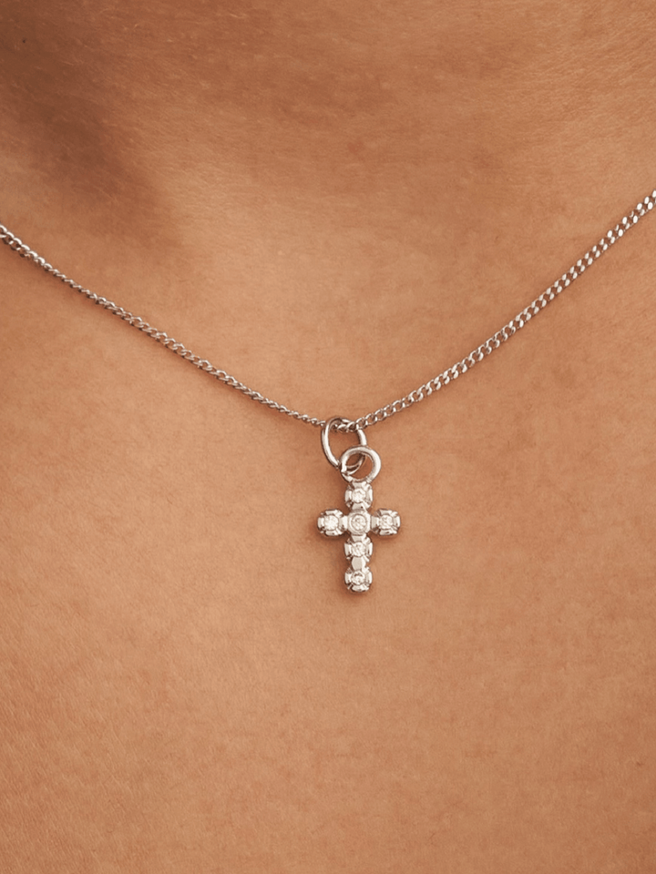 Silver cross necklace with clear stones on a person&