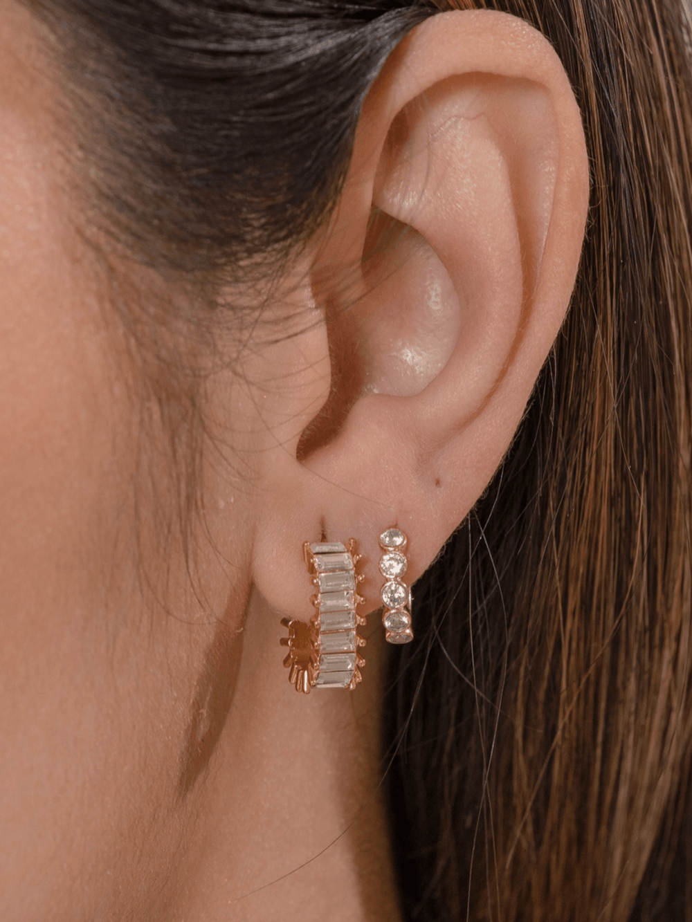 Close-up of an ear wearing gold and silver hoop earrings.