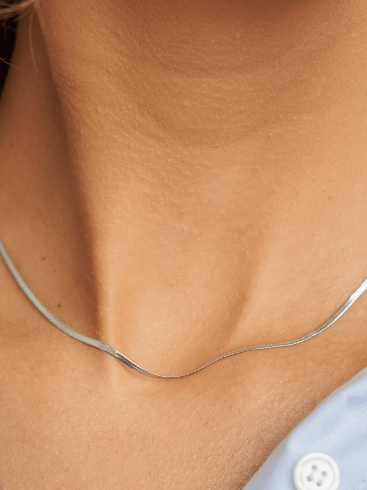Close-up of a person wearing a thin silver necklace on a light skin background