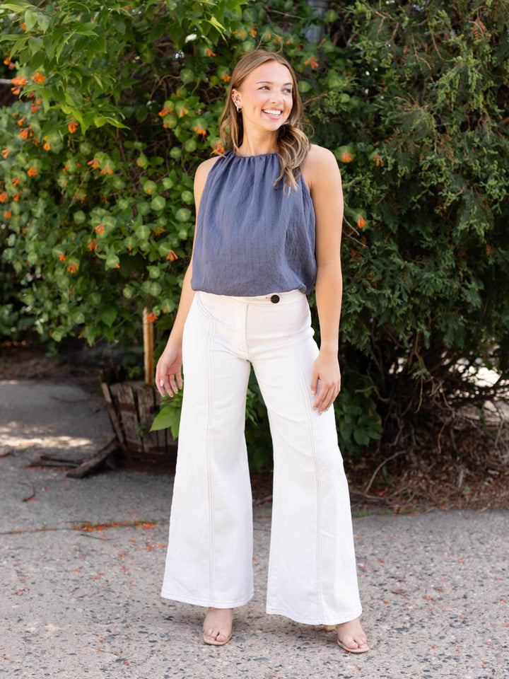 Model wears a flowy navy bubble striped tank top with white wide-leg pants.